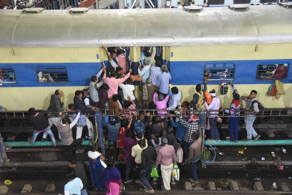 प्रयागराज में चल रहे महाकुंभ मेले के कारण रेलवे स्टेशन पर भीड़ के बीच यात्री ट्रेन के भीड़ भरे कोच में लटके हुए